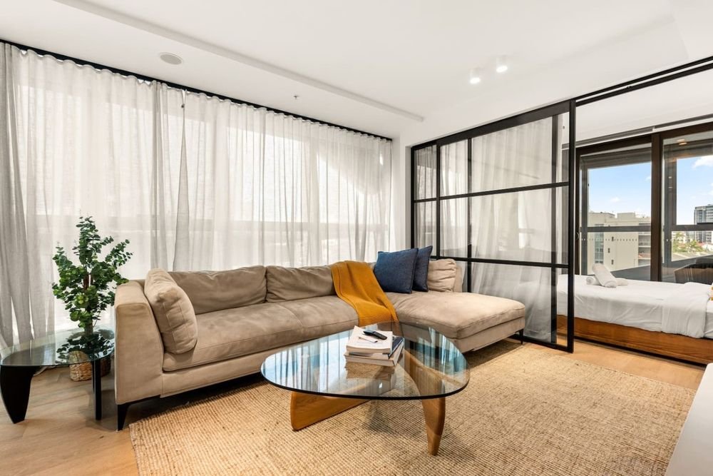 Living room with a long sofa and glass coffee table beside the glass-framed bedroom