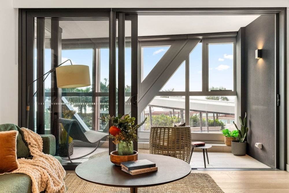 Living room with a green sofa and round coffee table, opening onto the enclosed balcony