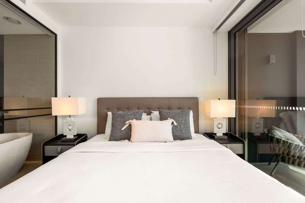 Bedroom with an upholstered bedhead, bedside lamps and a glass wall through to the bathroom
